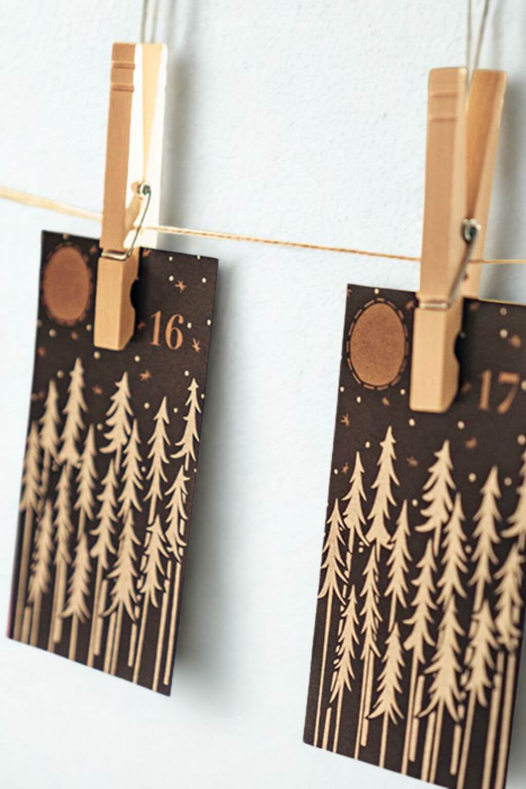 Advent calendar cards numbered sixteen and seventeen clipped to a string with wooden clothespins, featuring gold forest artwork.