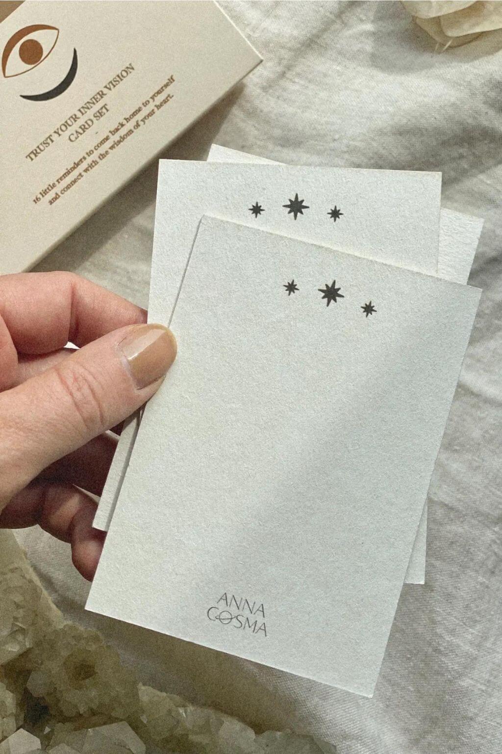 Hand holding the natural paper backs of Trust Your Inner Vision affirmation cards with small star illustrations