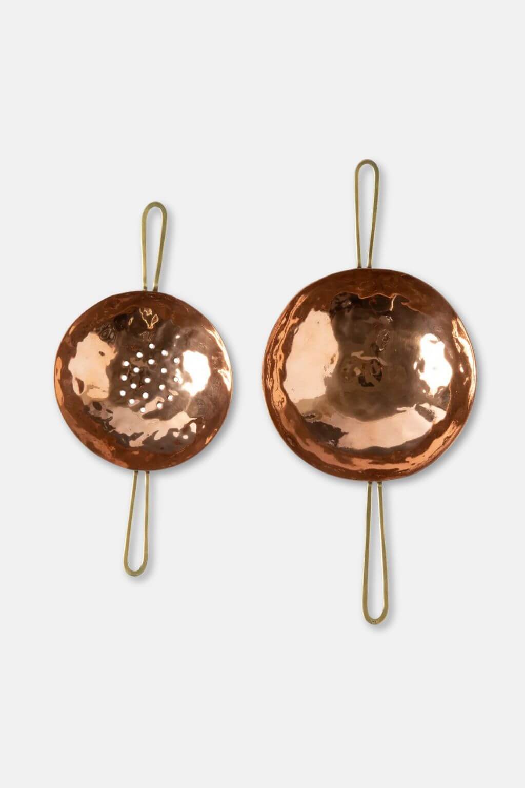 Two copper elements of a tea strainer with brass handles on a white background
