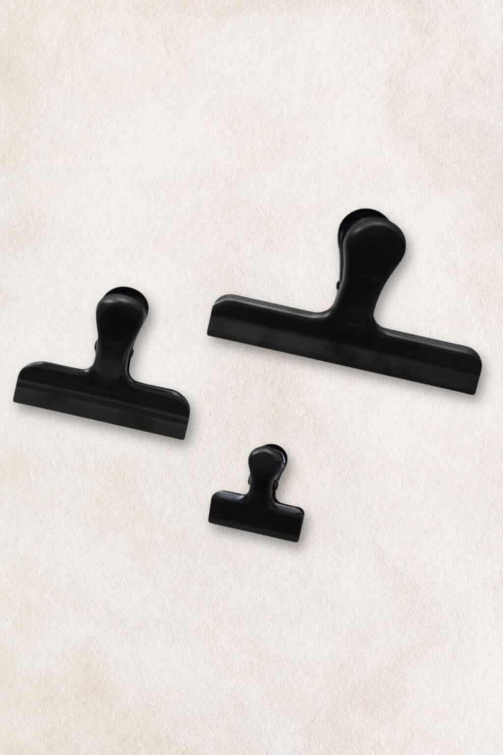 Three black binder clips in different sizes arranged on a textured off-white background.