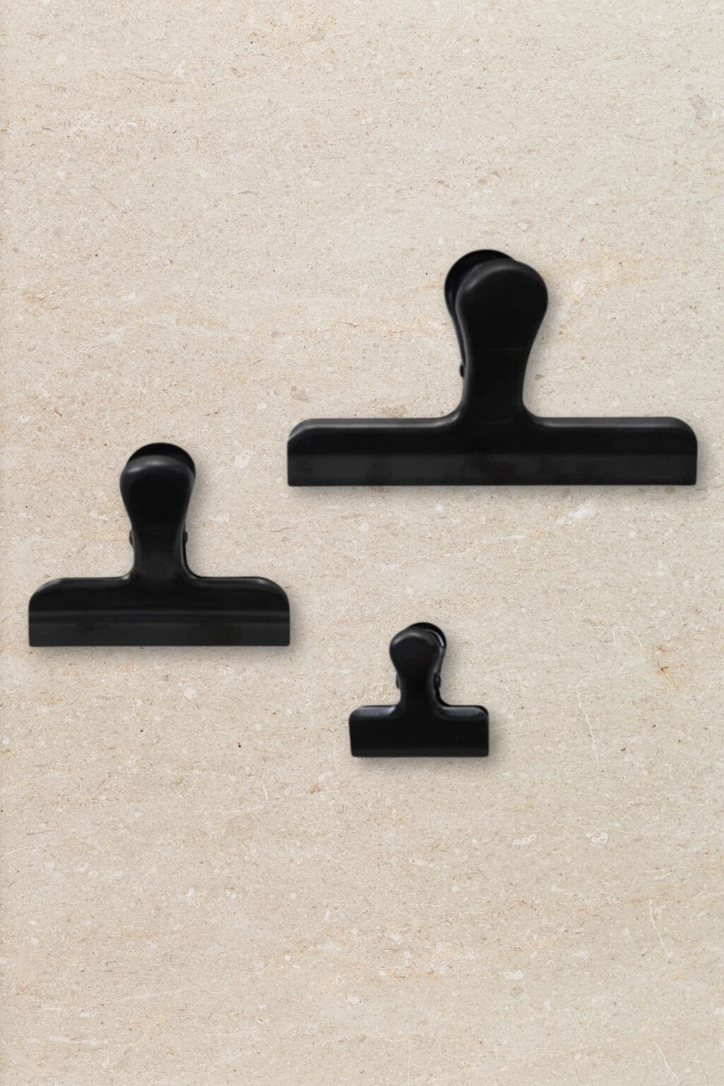 Three black binder clips in different sizes arranged on a textured beige background.