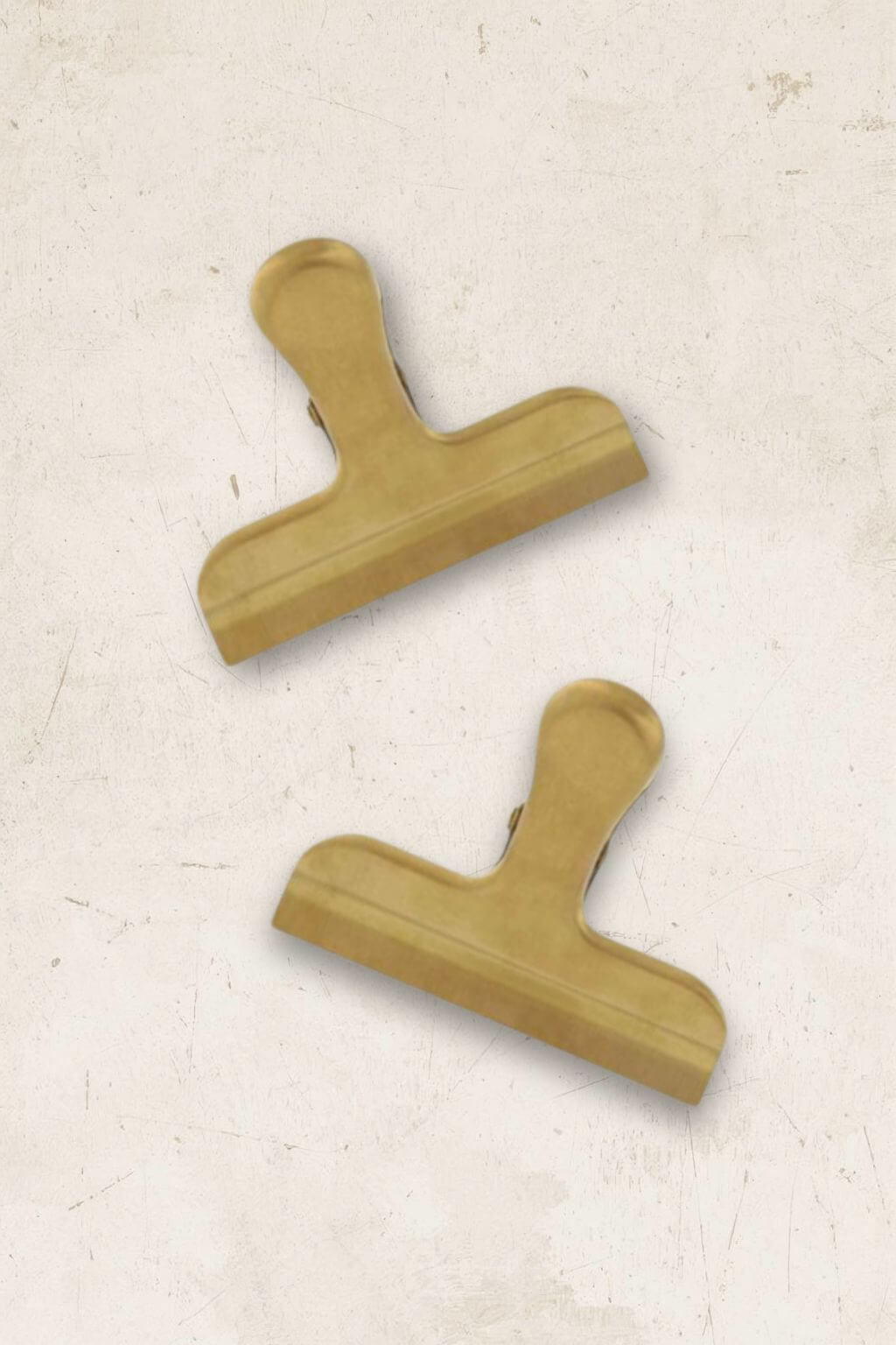 Two brass clips on a textured beige background.