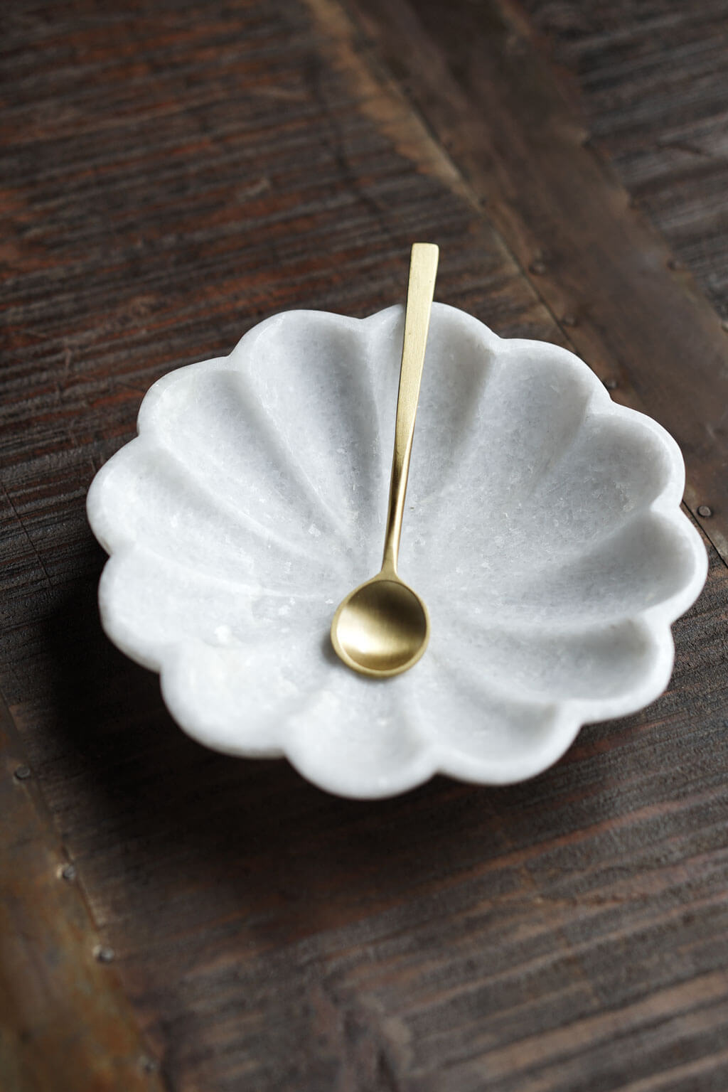 Marble fluted dish with scalloped edges holding a brass spoon on wooden surface
