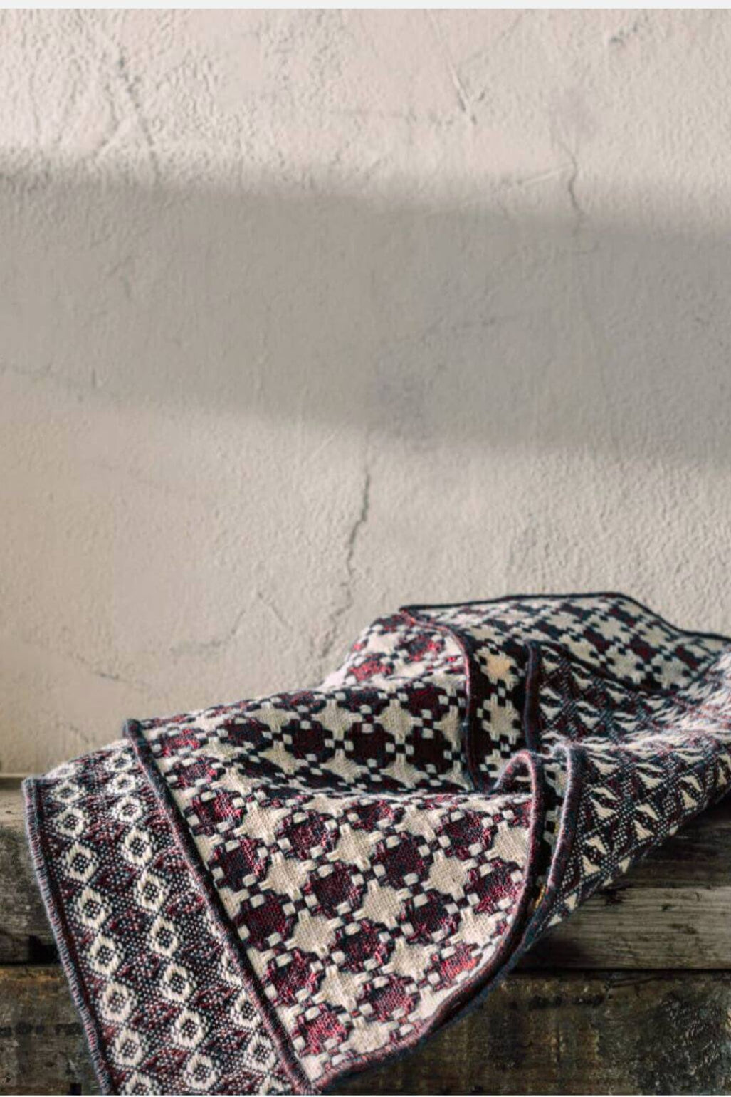 Patterned woven dishcloths draped over a wooden surface with a textured wall background
