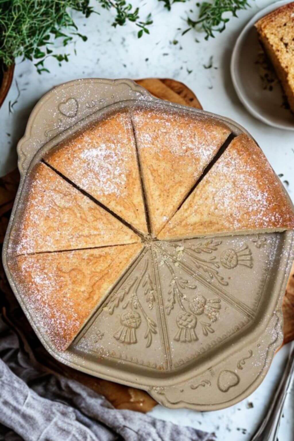 Decorative ceramic shortbread pan with a baked shortbread inside, dusted with powdered sugar.