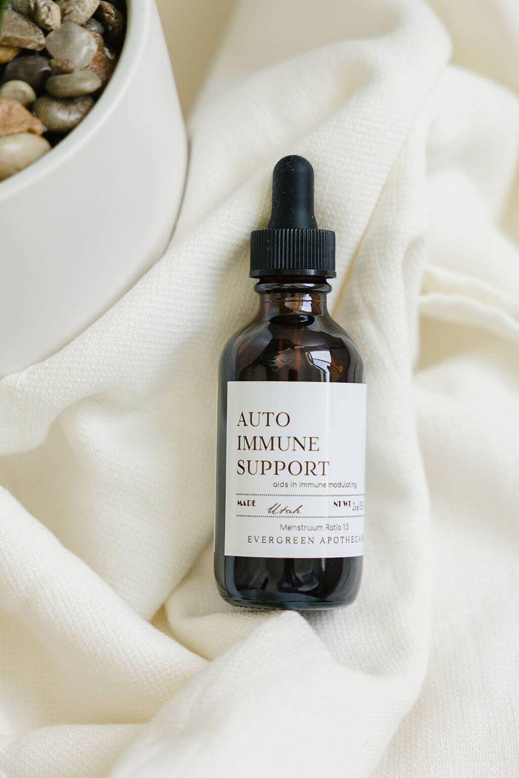 evergreen apothecary autoimmune support tincture on soft linen beside bowl of stones