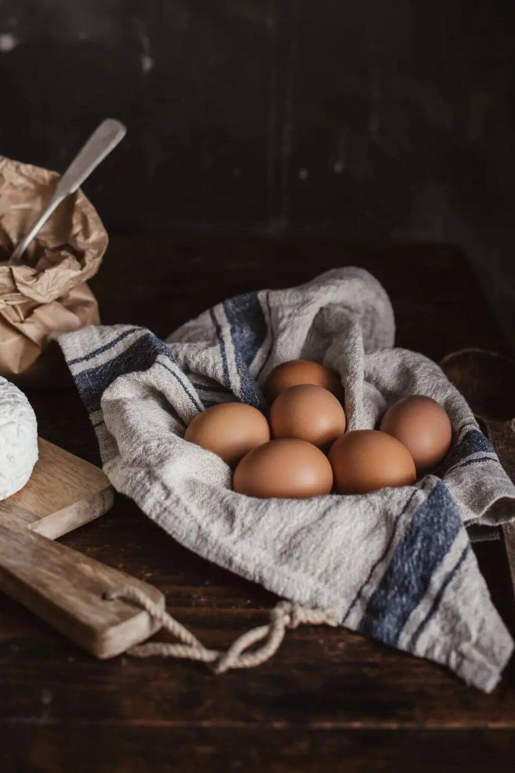 Blue stripe linen kitchen towel cradling fresh farm eggs in wooden bowl