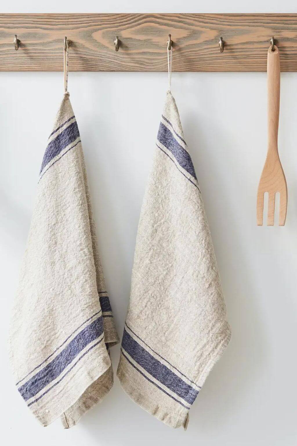 Blue stripe heritage linen kitchen towels hanging from wooden wall hooks