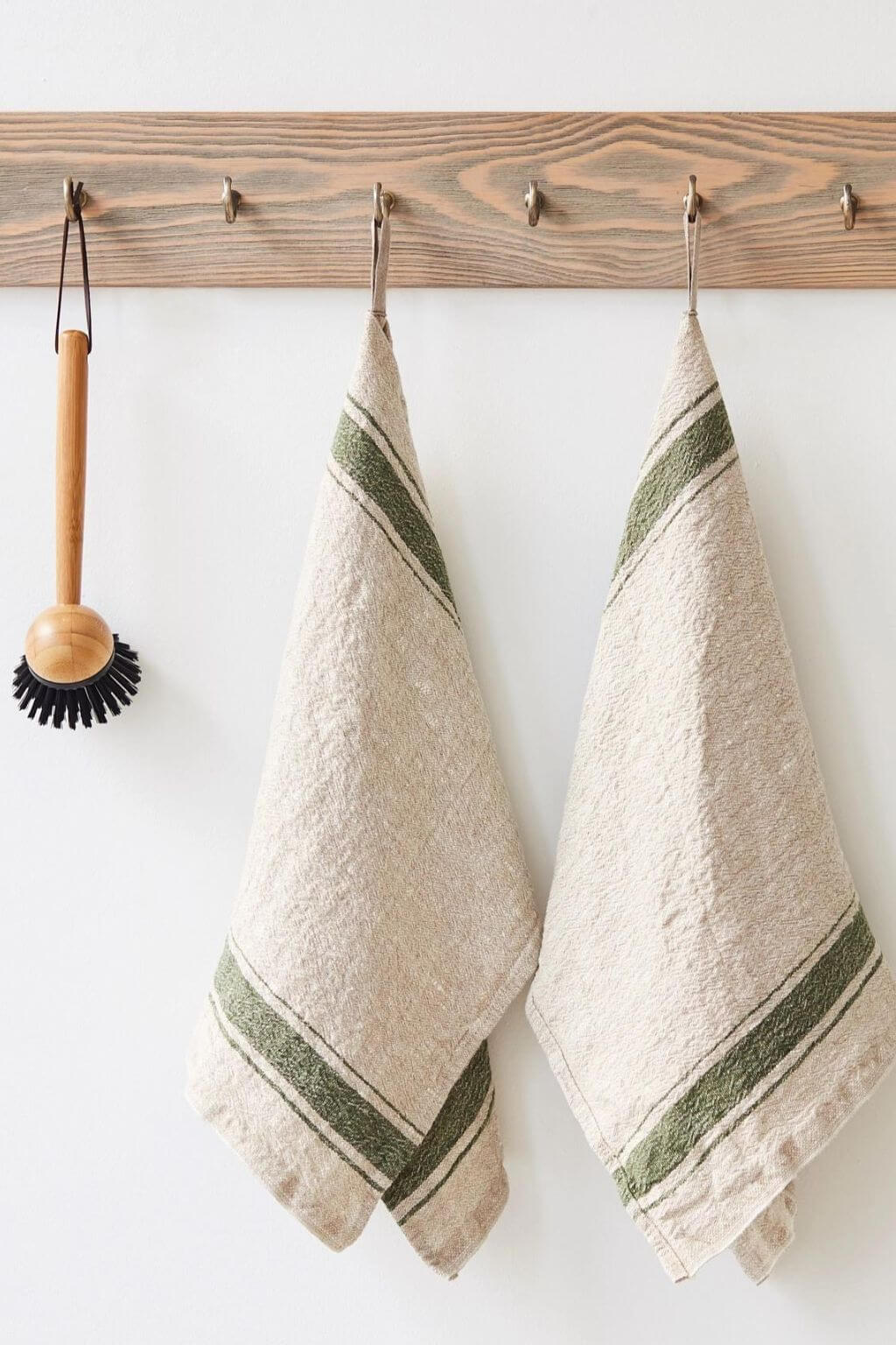Green stripe heritage linen kitchen towels hanging beside wooden dish brush
