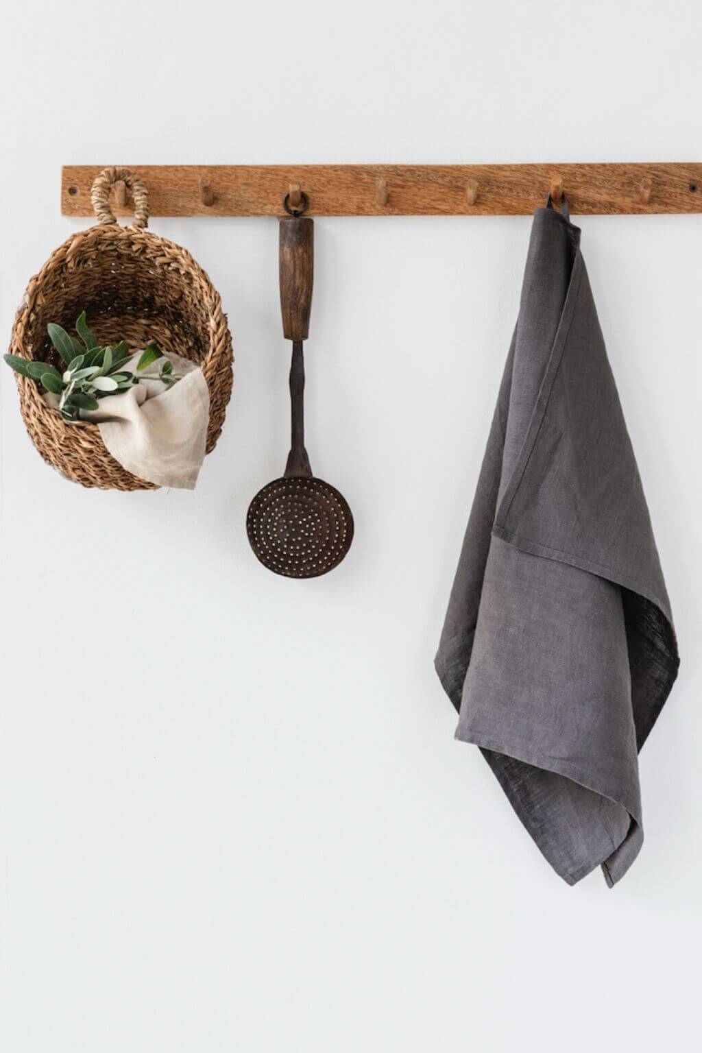 Wooden hook rack with a basket, towel, and ladle on a white wall