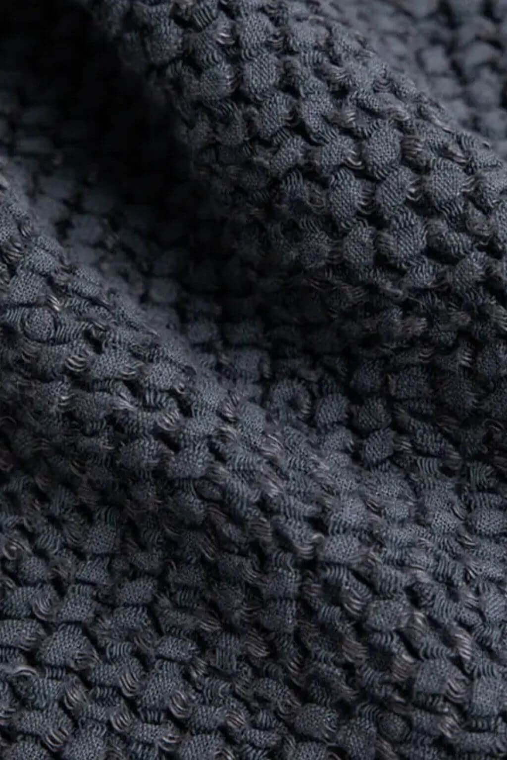 Close-up of a dark charcoal gray textured knit fabric with a ribbed and waffle-like pattern, showing soft folds and shadows.