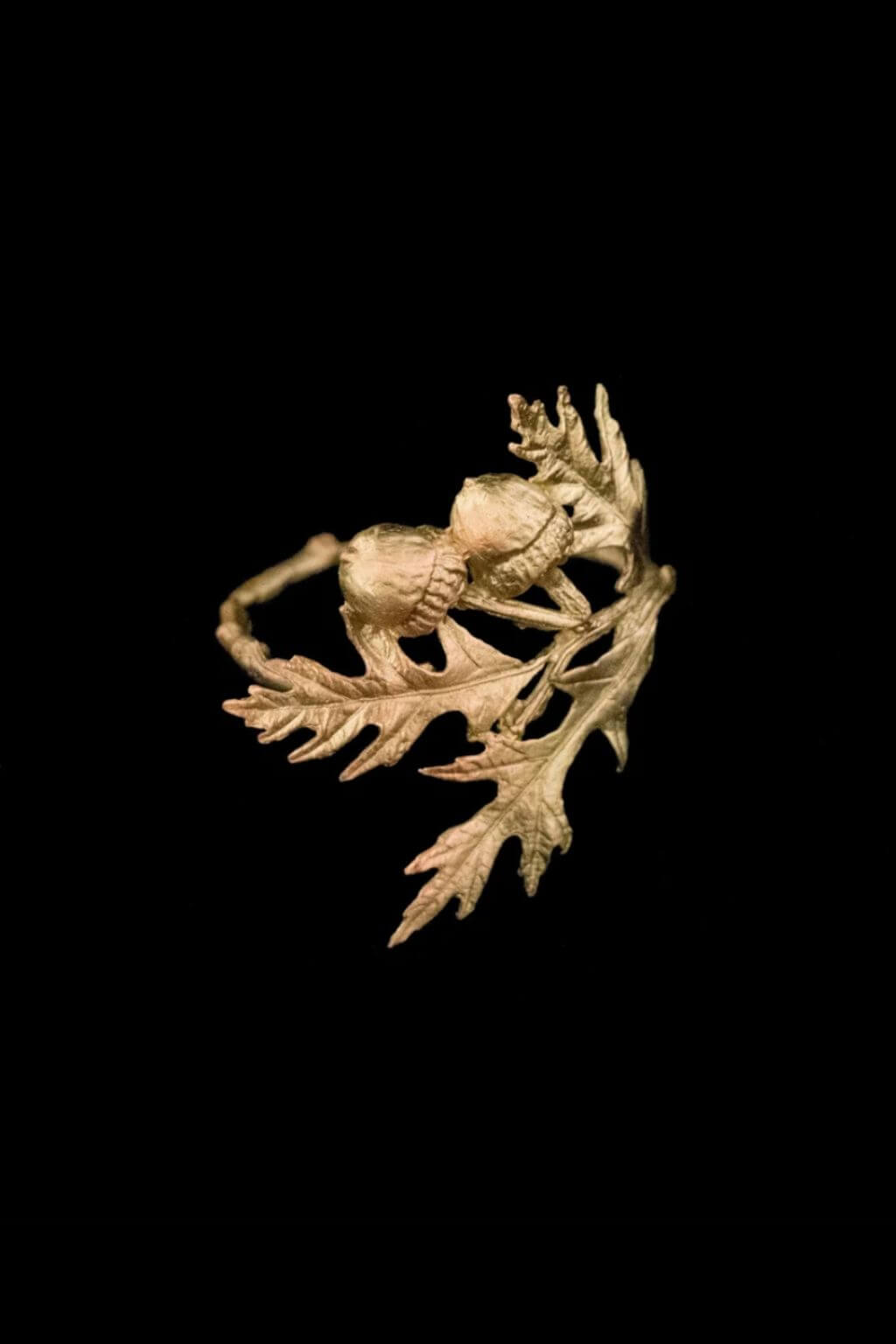 An artisan bronze naapkin ring sculpted in the shape of a oak leaaves and acorns shown against a solid black background.