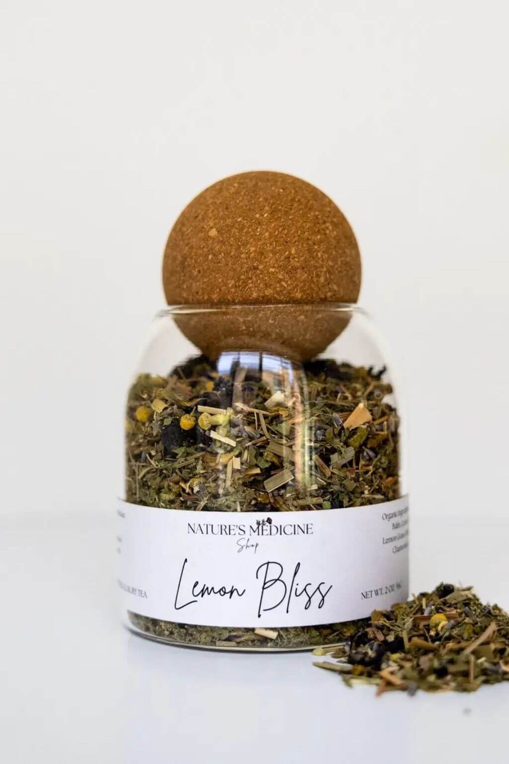 A glass jar of Nature's Medicine 'Lemon Bliss' steam with a cork stopper, shown on a clean white background with some loose herbal blend spilled in front.