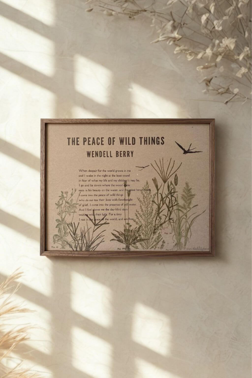 A framed wall art print featuring Wendell Berry's poem 'The Peace of Wild Things' with botanical illustrations, displayed on a textured beige wall with soft window shadows.