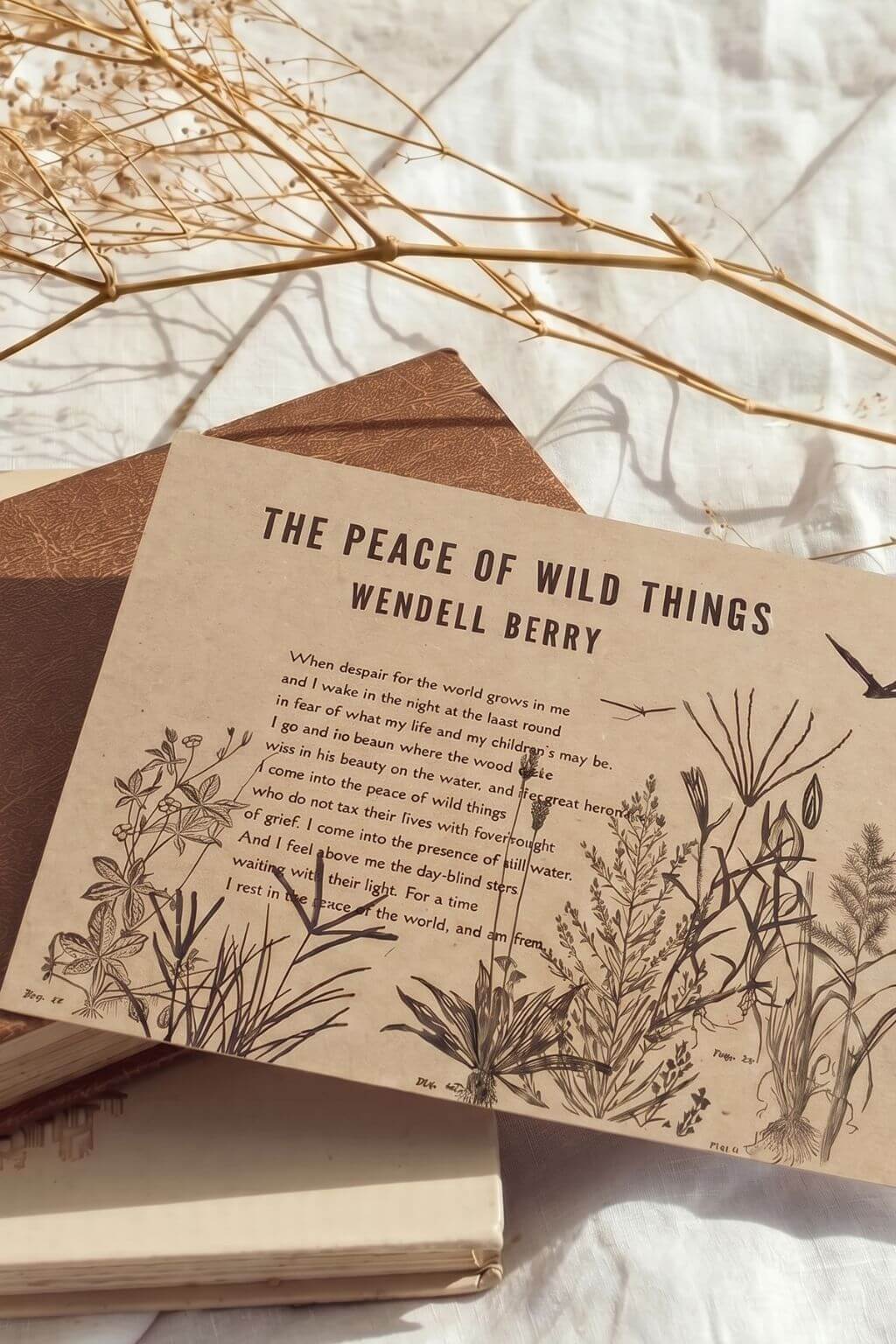 An art print featuring the poem 'The Peace of Wild Things' by Wendell Berry, styled on top of a vintage book with dried botanical branches in the background.
