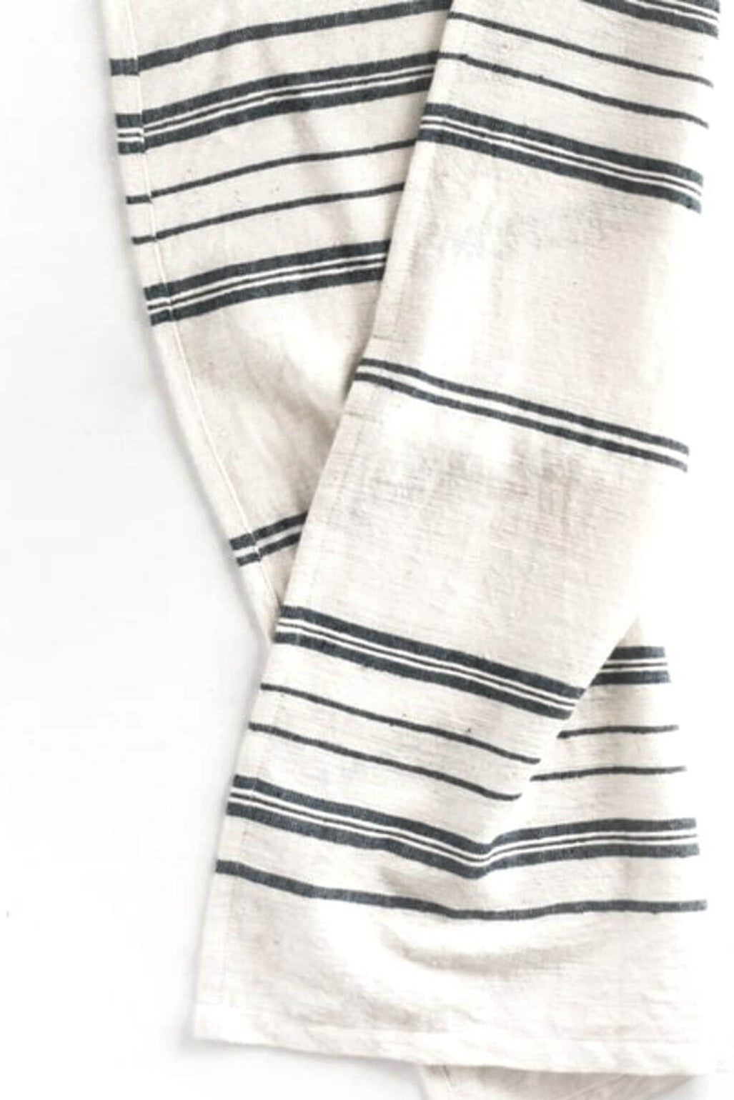 A close-up of a folded white tea towel with thin navy stripes