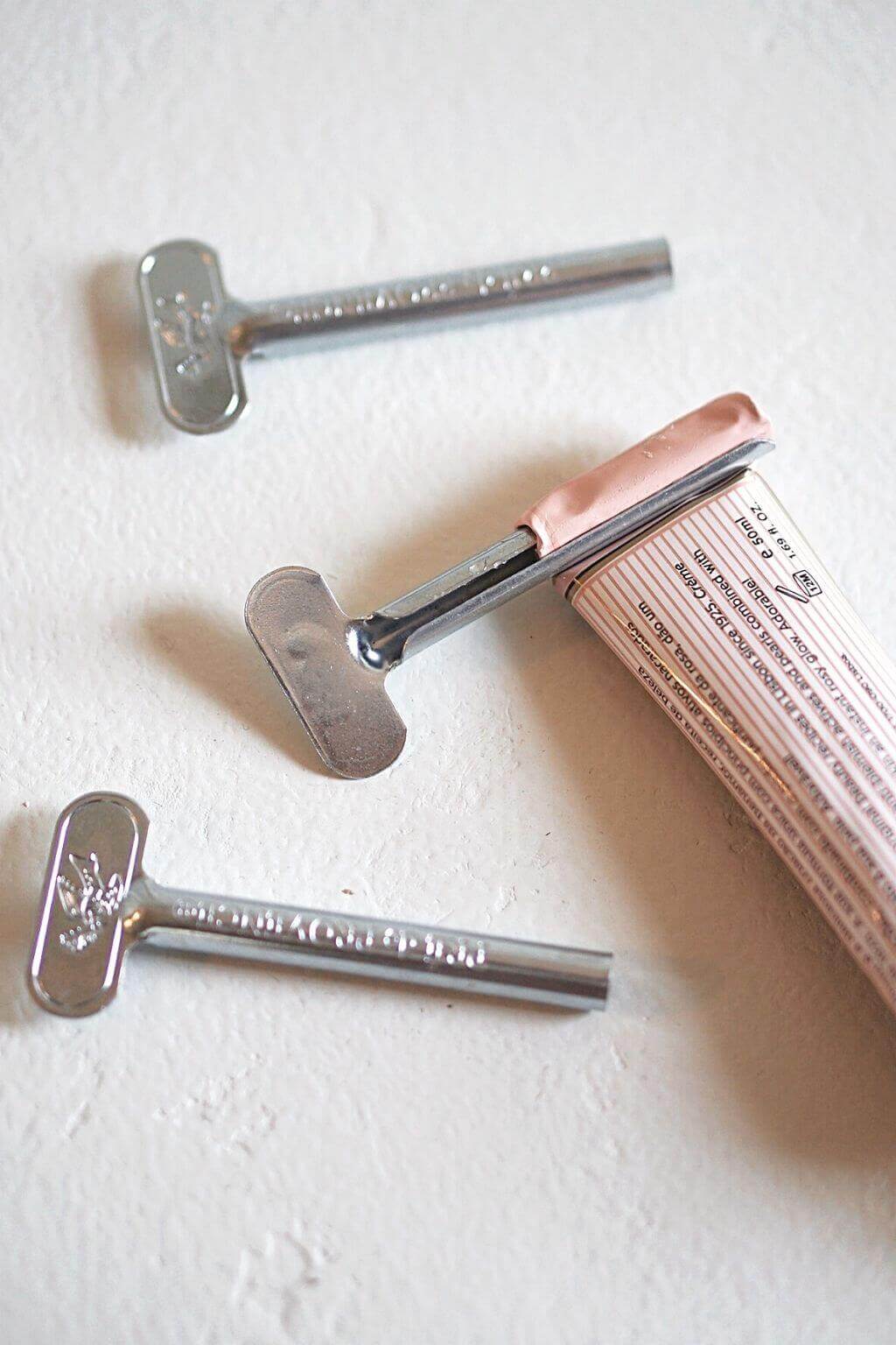 Two Metal Tube Roller Keys alongside a partially rolled cream tube, showing how the tool helps squeeze out every last drop of product.