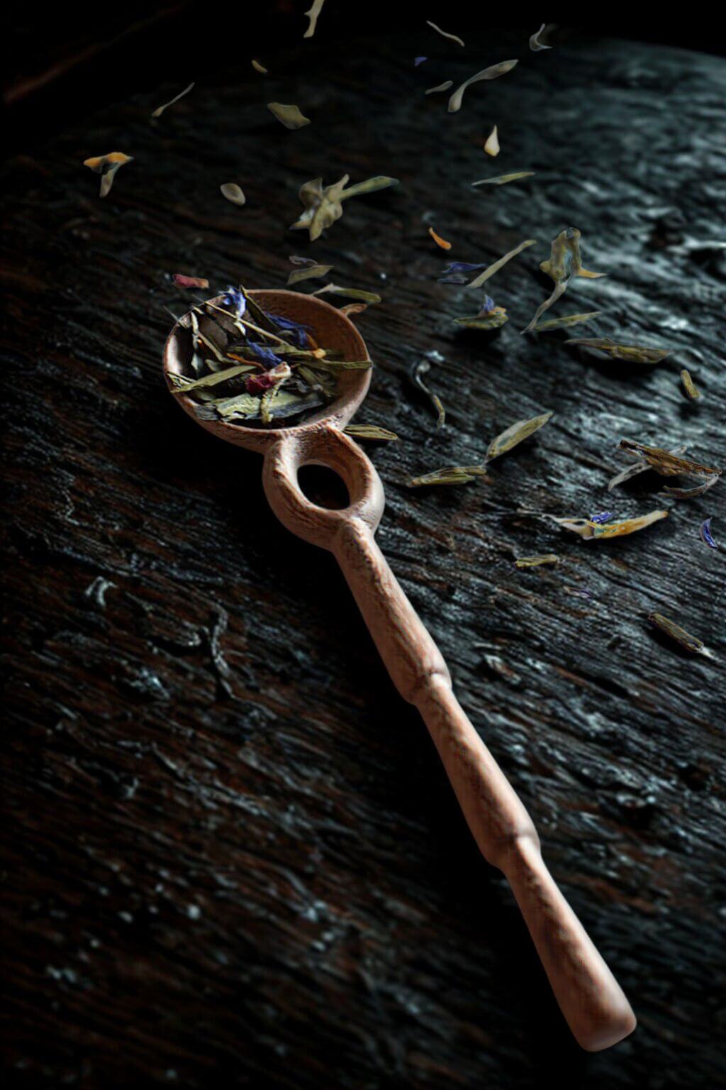 Doussie Wood Caravan Spoon with dried tea leaves on a dark wood surface