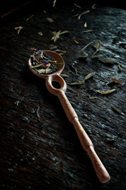 Doussie Wood Caravan Spoon with dried tea leaves on a dark wood surface