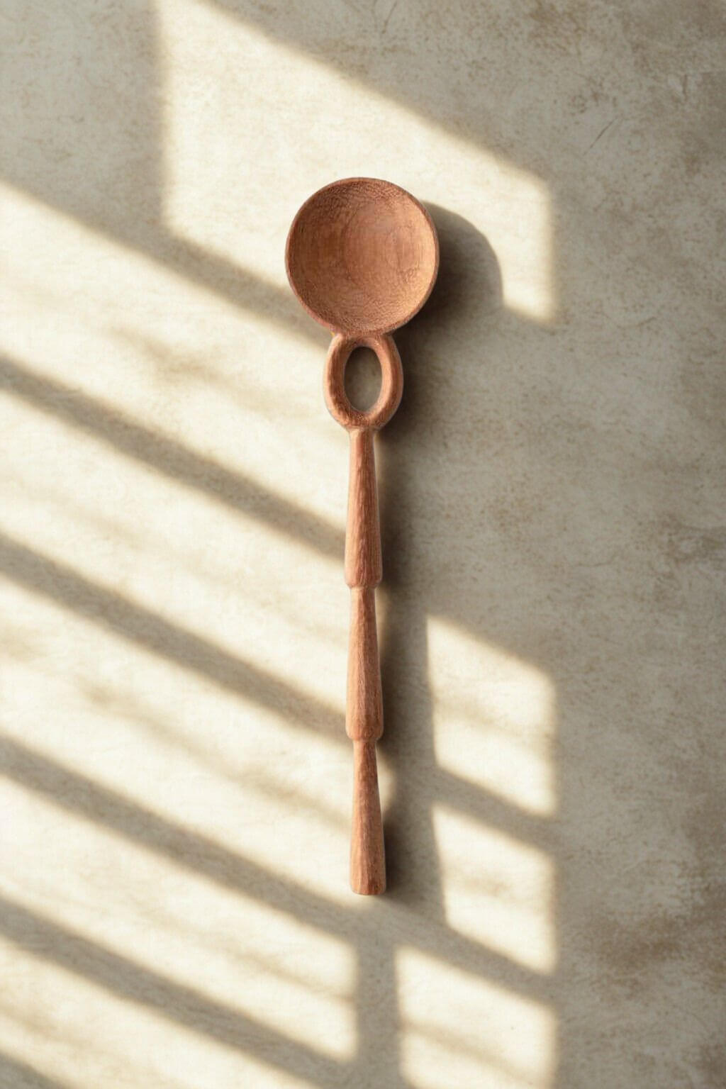 Wooden Caravan doussie wood spoon on a textured surface with sunlight casting shadows