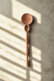 Wooden Caravan doussie wood spoon on a textured surface with sunlight casting shadows