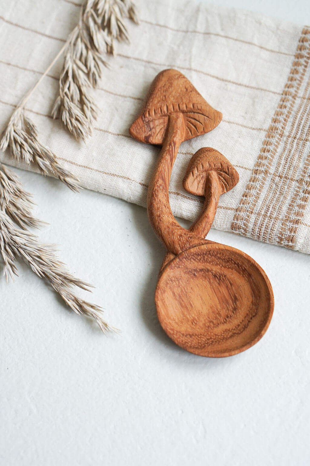 Hand-carved wooden mushroom spoon on linen cloth with dried grasses
