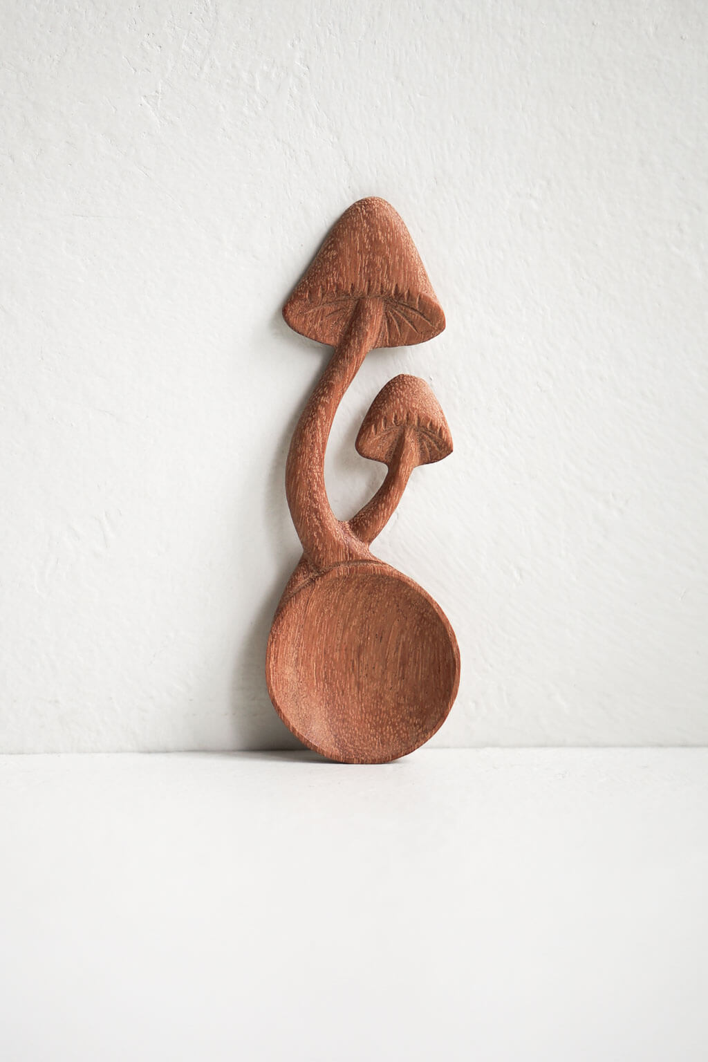 Hand-carved wooden mushroom spoon standing upright against neutral wall