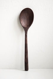 A large walnut handcrafted wooden spoon with a smooth finish and a long handle, displayed against a neutral background.