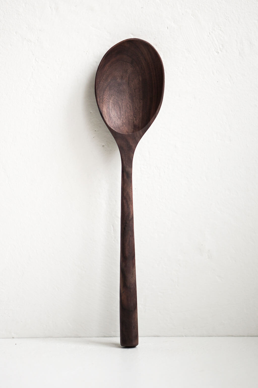 A large walnut handcrafted wooden spoon with a smooth finish and a long handle, displayed against a neutral background.