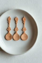 Three petite wooden spice spoons arranged on a ceramic plate