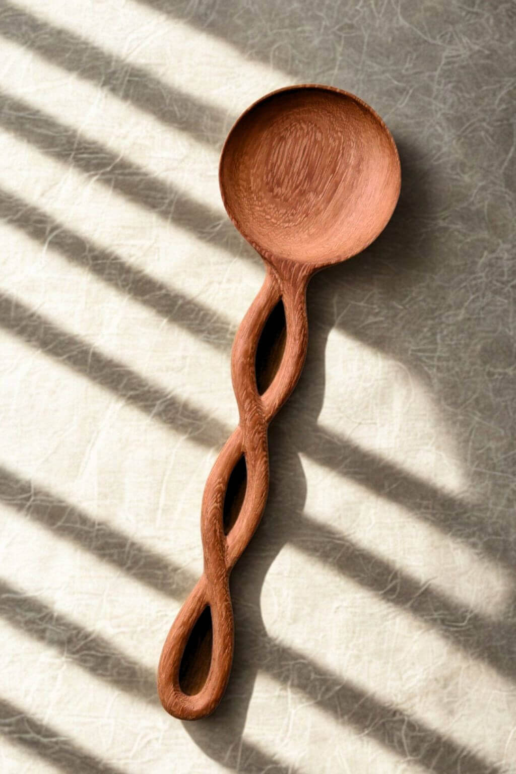 Hand Carved Doussie Wood Spoon with a twisted handle on a textured surface with natural light streaming in