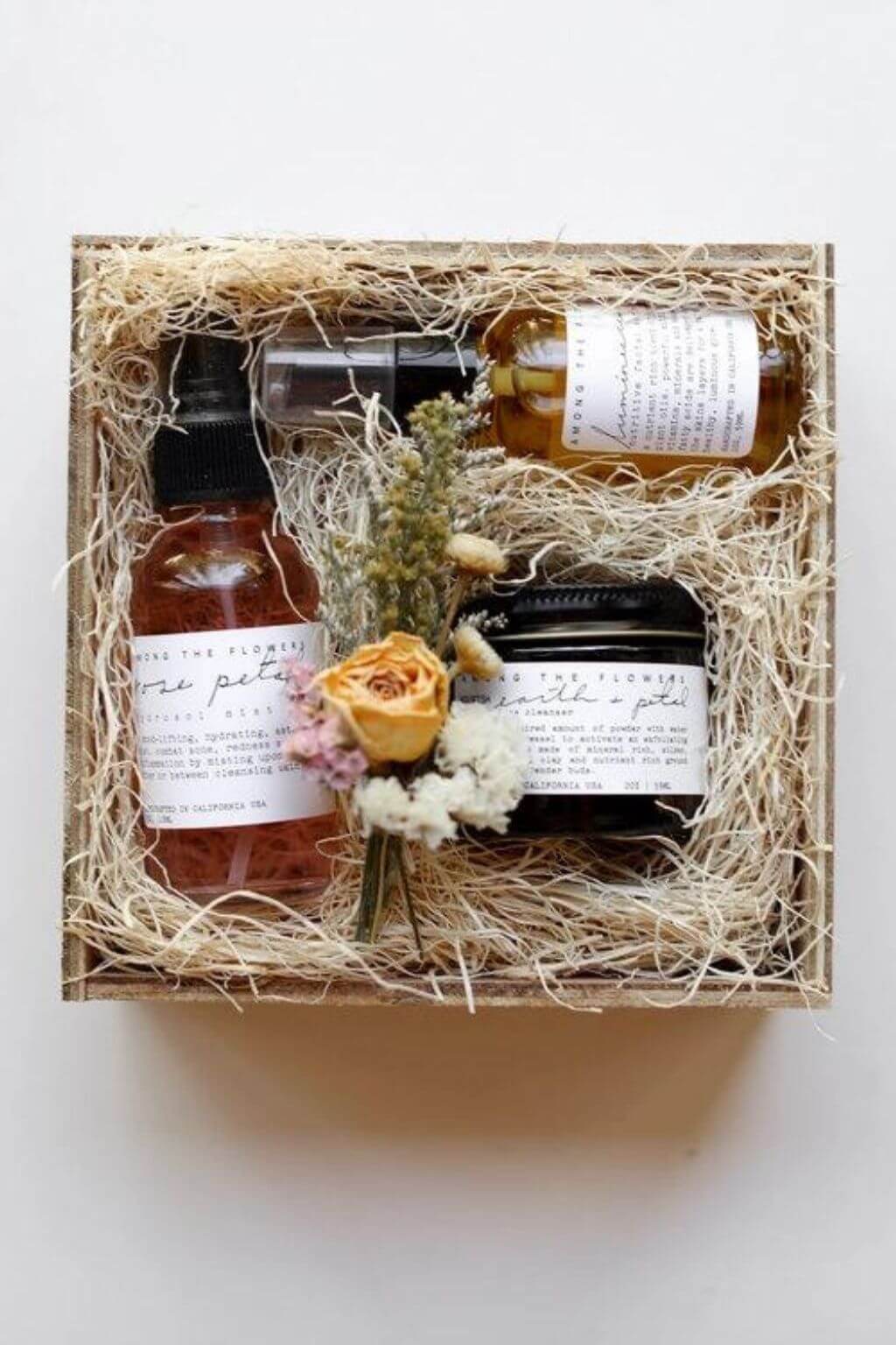 Botanical self-care gift set with floral bath oil, body scrub, and mist arranged in a straw-filled box with dried flowers