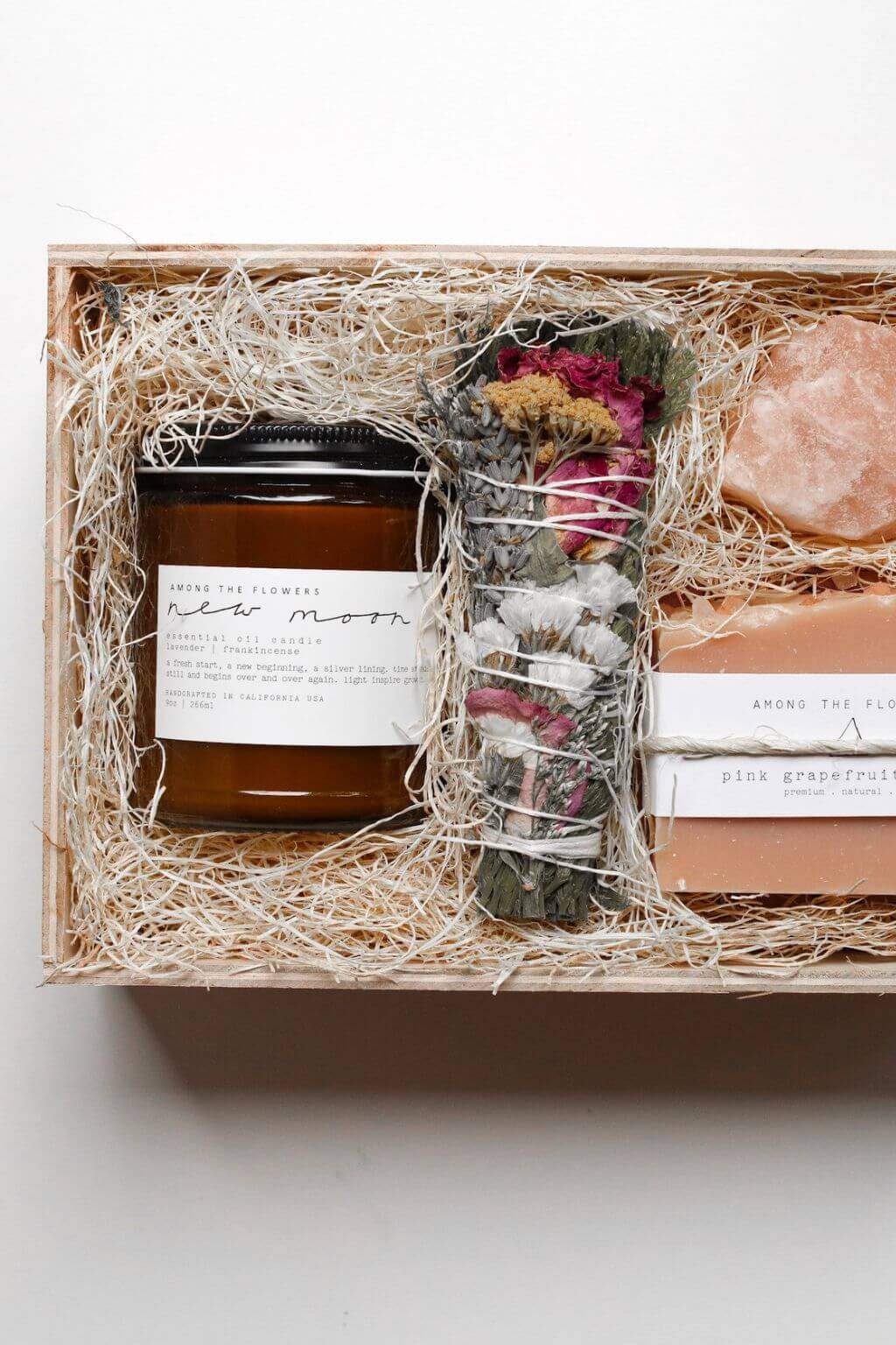 Botanical gift set with amber candle, floral smudge bundle, and handmade soap arranged in a straw-filled wooden box