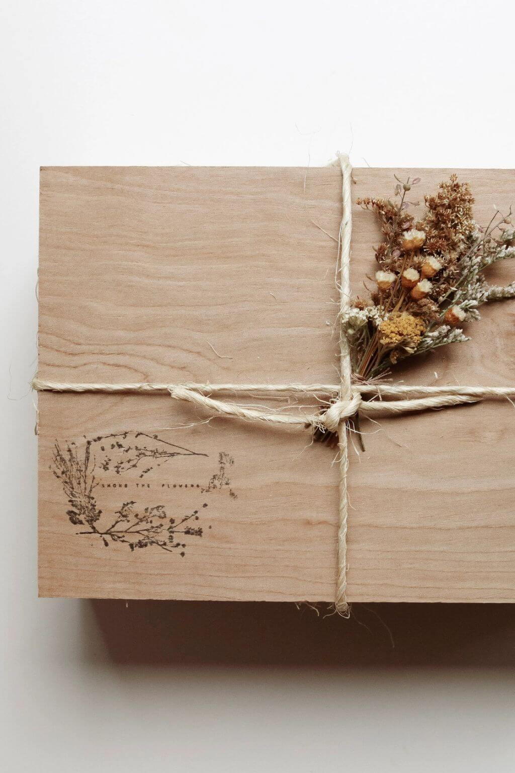 Wooden gift box tied with twine and adorned with dried flowers, featuring botanical branding on lid