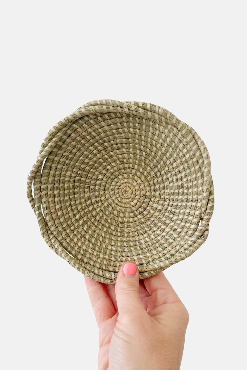 Hand holding a woven circular basket against a plain background