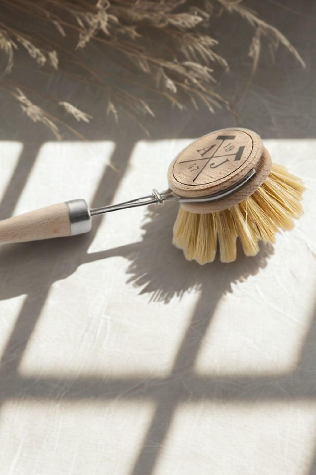 Dish brush with wooden handle on a textured surface with natural light casting shadows.