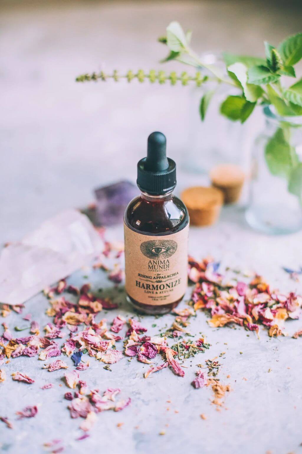 A bottle of Anima Mundi Harmonize Tonic with rose petals and crystals in the background