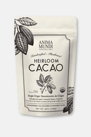 A pouch of Anima Mundi Apothecary Heirloom Cacao, featuring a cream-colored background with black botanical illustrations of cacao pods and leaves, and black text on the front label.
