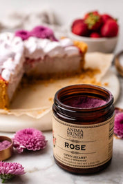 An open amber glass jar of Anima Mundi Rose Powder by Anima Mundi Apothecary, set on a marble surface with a blurred slice of berry pie and fresh strawberries in the background.