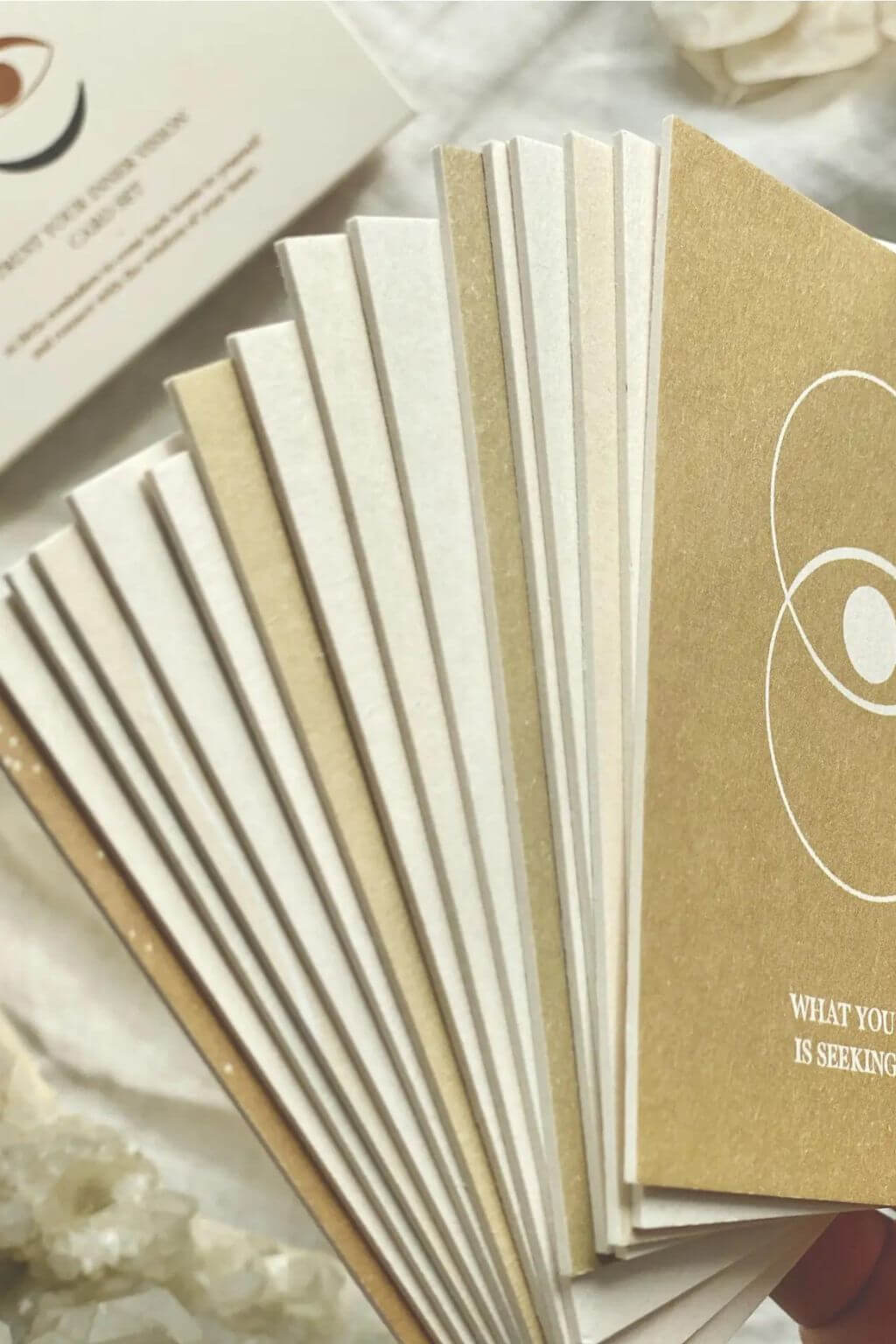 Fanned edges of natural paper affirmation cards beside a card reading What You Seek Is Seeking You