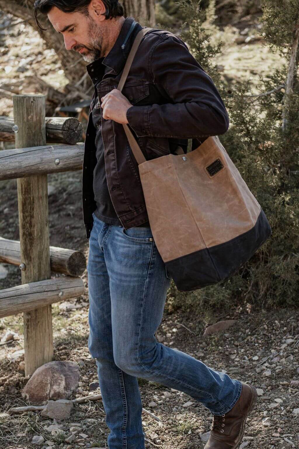 Man carrying oversized waxed canvas tote bag on shoulder outdoors