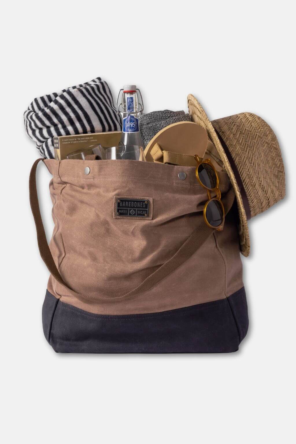Brown backpack with black bottom section, containing a hat, sunglasses, bottle, and other items on a light gray background.