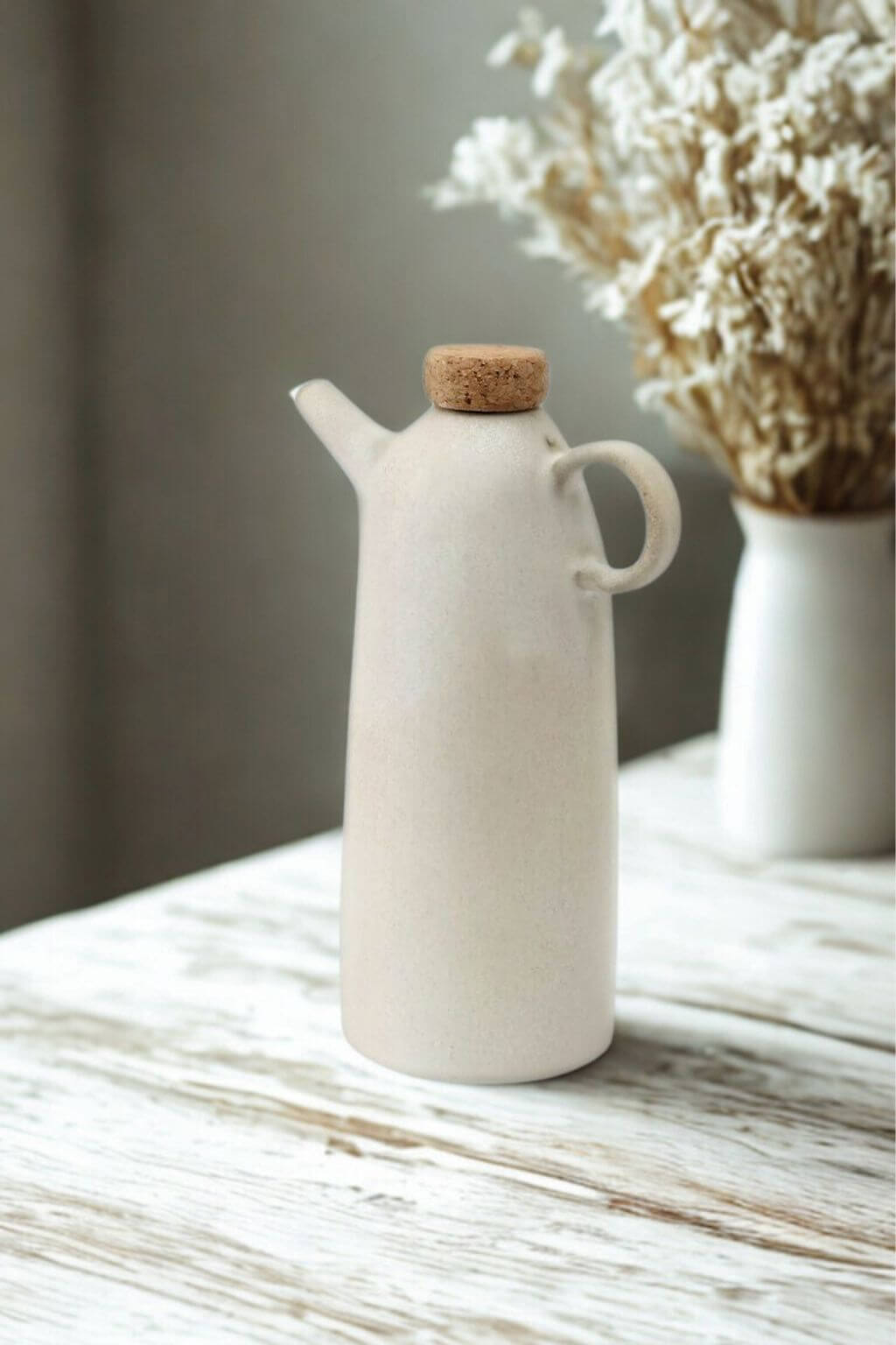 White ceramic olive oil bottle with dried flowers background