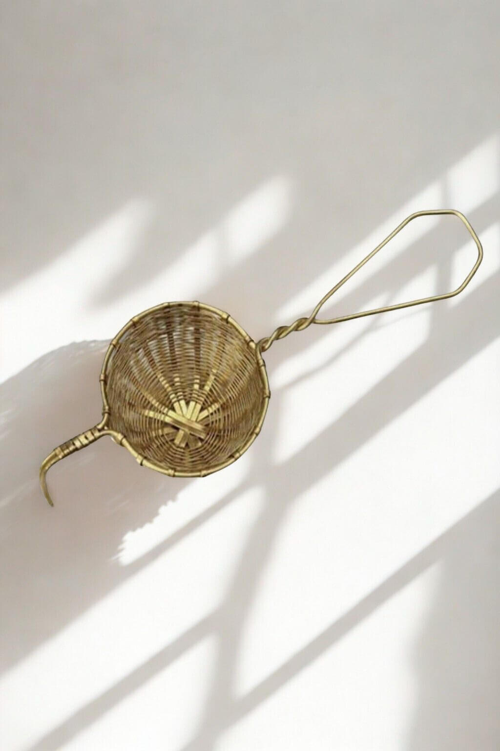 Solid brass loose leaf tea infuser with woven basket detail on white background with shadows