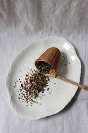 Loose leaf Cloud Nine herbal tea blend with bamboo scoop on an elegant ceramic plate
