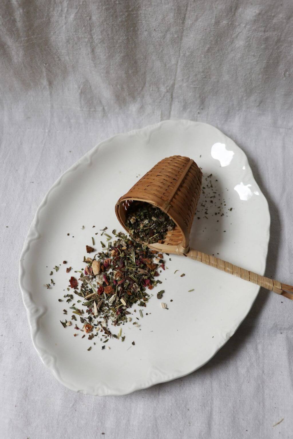 Loose leaf Cloud Nine herbal tea blend with bamboo scoop on an elegant ceramic plate