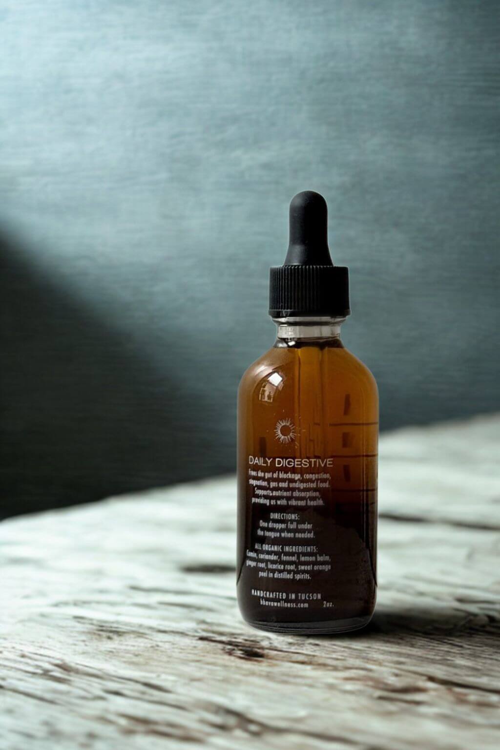 Bottle of Daily Digestive Herbal Tincture on a rustic wooden surface with a slate gray background