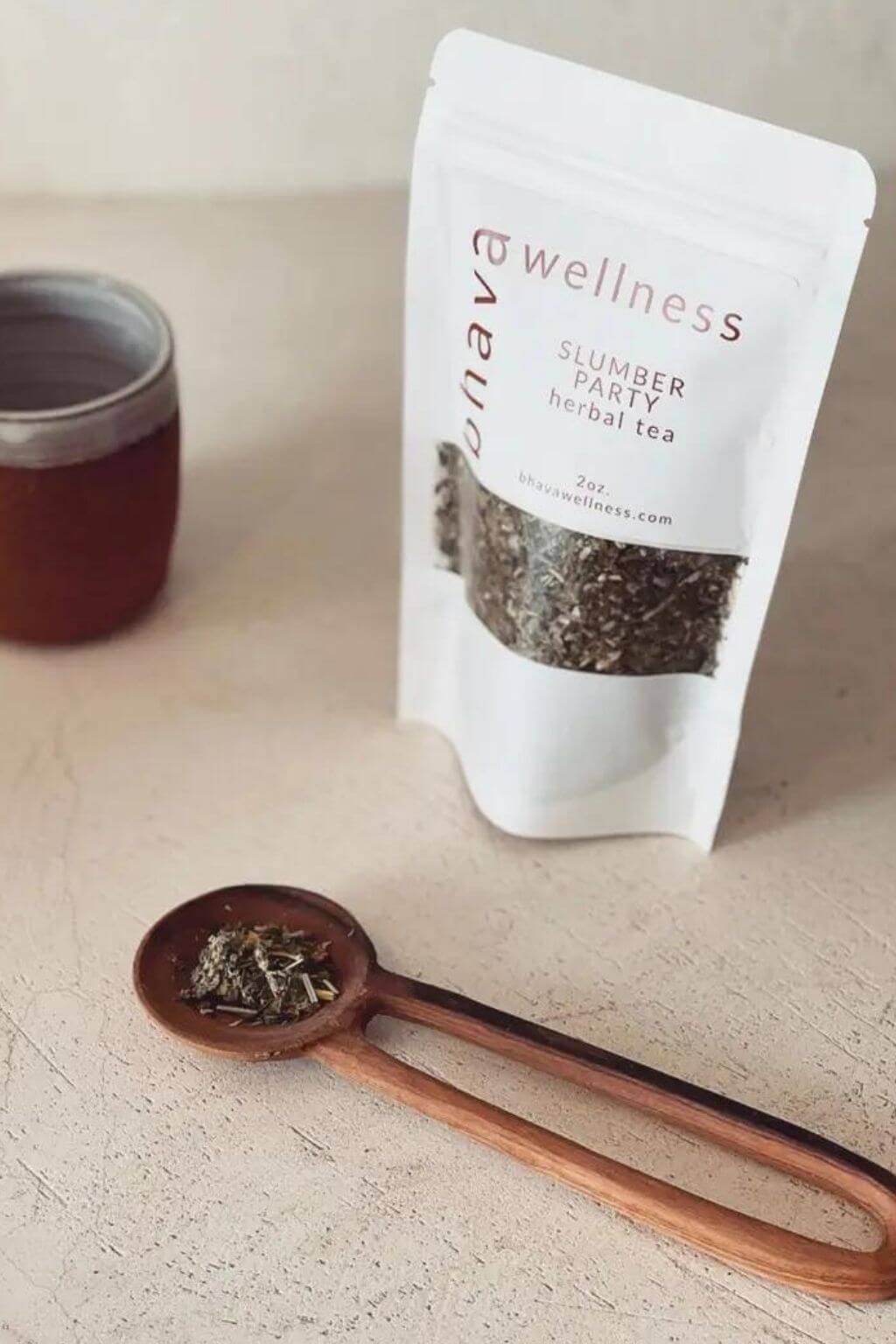 Bhava Wellness Slumber Party Herbal Tea package with a wooden spoon and tea leaves on a light surface.