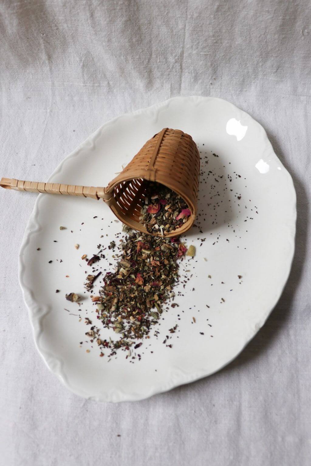Loose herbal tea blend spilling from bamboo scoop