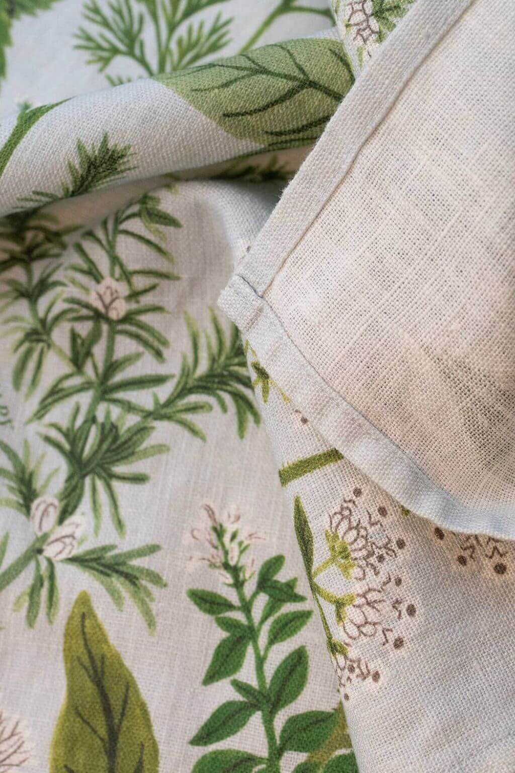 Detail of Herb Garden Linen Tea Towel fabric, showing natural linen texture and delicate green herb illustrations with stitched edges.